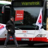 Ein streikender Busfahrer läuft mit einer Flagge der Gewerkschaft Verdi an einem Bus vorbei.