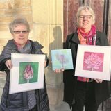 Magdalena Starke und Gisela Rott (r.) zeigen zwei Bildmotive und den Bildband „Dem Leben lauschen“ vor der Pforte der Waltroper Petruskirche.