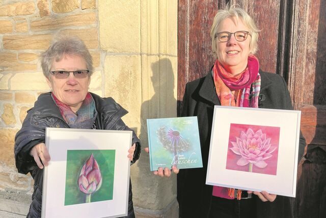 Magdalena Starke und Gisela Rott (r.) zeigen zwei Bildmotive und den Bildband „Dem Leben lauschen“ vor der Pforte der Waltroper Petruskirche.