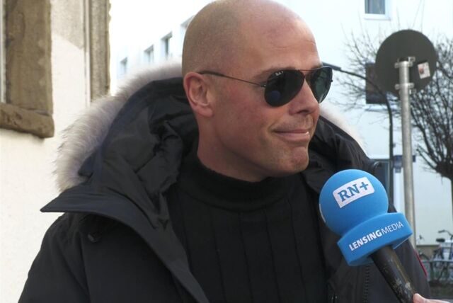 Ein Mann mit einer Sonnenbrille spricht bei einer Umfrage in ein Mikrofon mit RN-Logo
