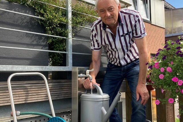 Ein Mann mit der Gießkanne vor einem Brunnen.