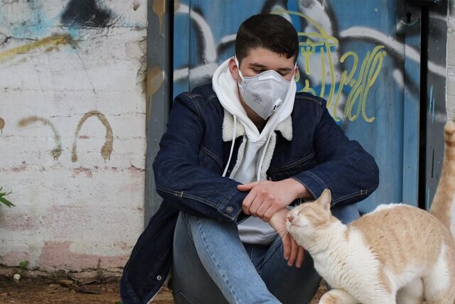 Ein junger Mann mit Maske streichelt eine Katze. Ein Foto aus Corona-Tagen.