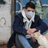 Ein junger Mann mit Maske streichelt eine Katze. Ein Foto aus Corona-Tagen.
