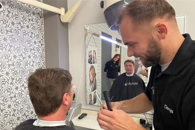 Denys schneidet einem Mann die Haare. Seine Chefin Heike Künkler schaut interessiert zu.