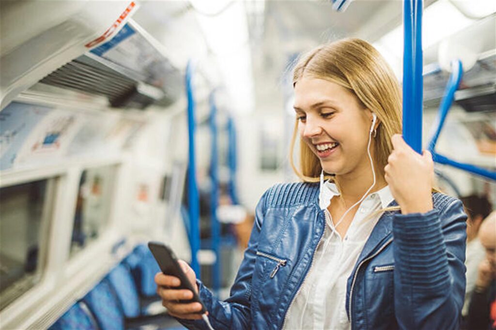 frau hört etwas von ihrem handy in der bahn und lacht