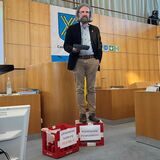 Daniel Molloisch seht im Ratssaal auf zwei Cola-Kisten.