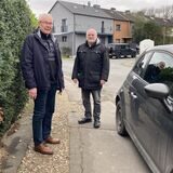 Zwei Senioren stehen zwischen einem Auto und einer Hecke auf einem Fußweg.