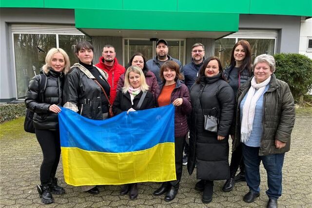 Ukrainerinnen und Ukrainer stehen vor dem Redaktionsgebäude in Marl. Drei von ihnen halten die Landesflagge in die Kamera.
