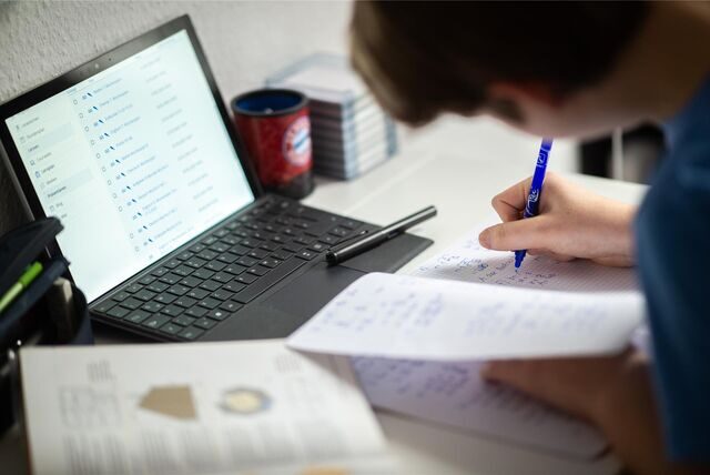 Ein Schüler sitzt in seinem Zimmer am Schreibtisch und erledigt Aufgaben, vor ihm steht ein Laptop.
