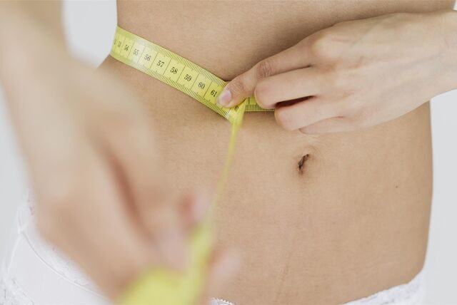 Eine Frau in Unterwäsche schlingt ein Maßband um ihren Bauch und misst ihren Bauchumfang