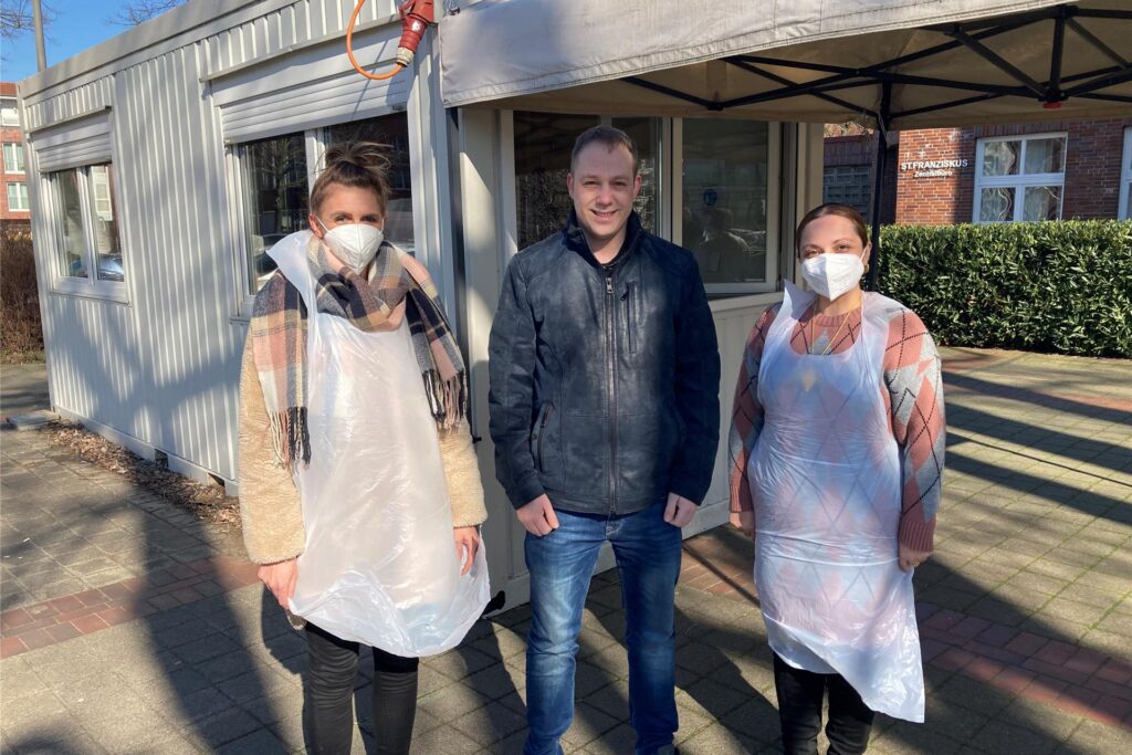 Drei Menschen stehen vor einem Corona-Testzentrzum.