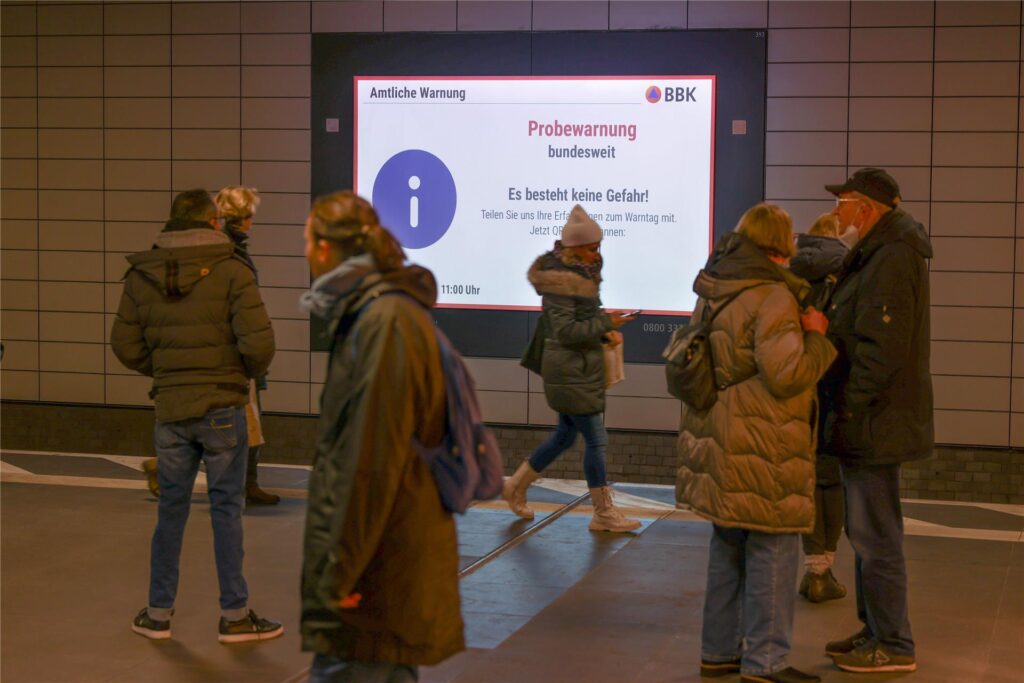 Eine Warnmeldung wird probeweise am S-Bahnhof Friedrichstraße auf einem digitalen Screen angezeigt, während eine S-Bahn einfährt.