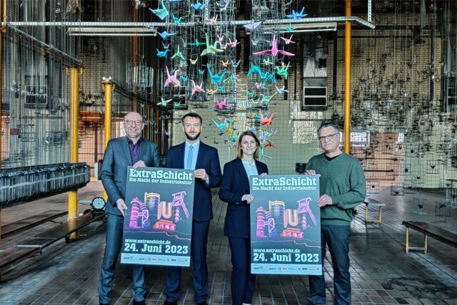 Vier Personnen in der Kaue der Zeche Westerholt werben mit Plakaten für die Extraschicht: Axel Biermann, Oliver Klatt von der RAG-Stiftung, Sandra Nierfeld von der RAG Montan Immobilien und Bernd Lohse. Das Quartett steht unter einer Installation der Künstlerin Chiara Dahlem.