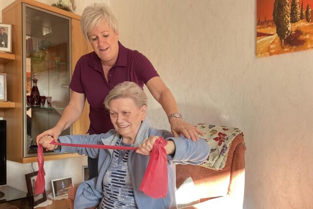 Claudia Geltenpoth macht einen Hausbesuch bei einer Patientin. Die Physiotherapeutin übt mit ihr an einem Gymnastikband.