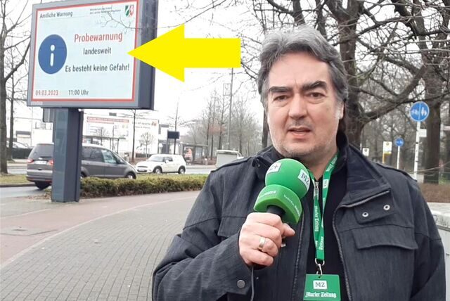 Ein Reporter mit einem Mikrofon in der Hand steht an einer Kreuzung.