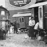 Das historische Bild zeigt eine Frau und ein Kind vor von Pferden gezogenen Wohnwagen.