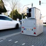 Ein weißes Auto fährt an einem Panzerblitzer der Stadt Herten vorbei.