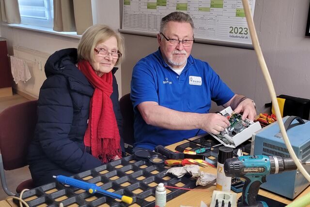 Ein Mann und eine Frau sitzen vor einer Werkbank und reparieren ein altes Radio.