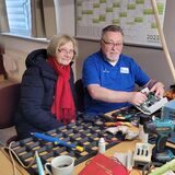 Ein Mann und eine Frau sitzen vor einer Werkbank und reparieren ein altes Radio.