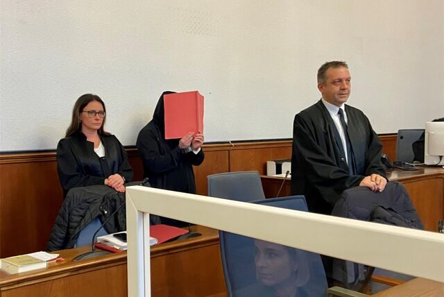 Der Angeklagte verbirgt sein Gesicht hinter einer Aktenmappe.