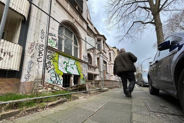 Ein Mann geht an einem mit Graffiti beschmierten Haus hinter einem Bauzaun lang