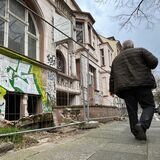 Ein Mann geht an einem mit Graffiti beschmierten Haus hinter einem Bauzaun lang