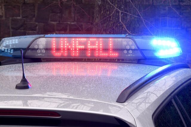 Blaulicht leuchtet bei Nacht an der Warnleuchte auf dem Dach eines Polizeiautos, in rot leuchtenden Buchstaben steht Unfall darauf geschrieben.