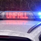 Blaulicht leuchtet bei Nacht an der Warnleuchte auf dem Dach eines Polizeiautos, in rot leuchtenden Buchstaben steht Unfall darauf geschrieben.