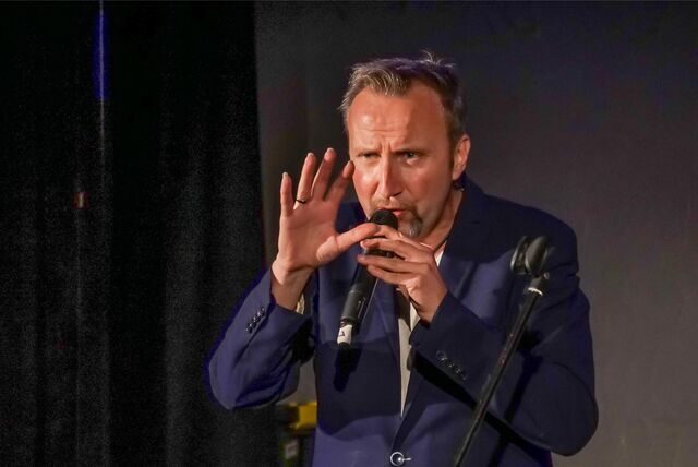 Moderator Helmut Sanftenschneider spricht in ein Mikrofon.