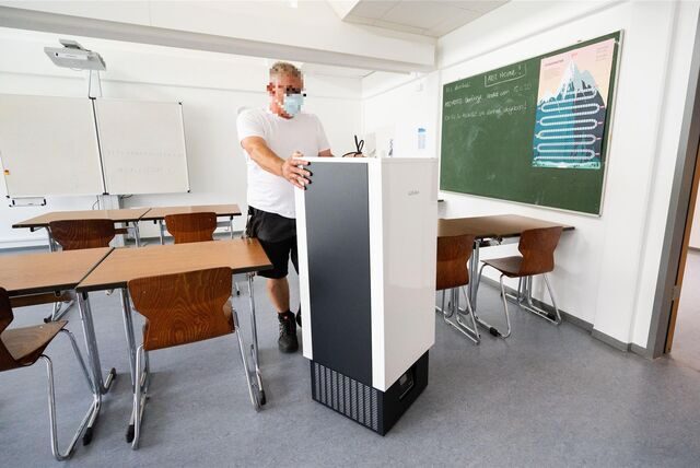 Ein Schulhausmeister installiert einen Luftfilter in einem Klassenraum.