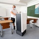 Ein Schulhausmeister installiert einen Luftfilter in einem Klassenraum.