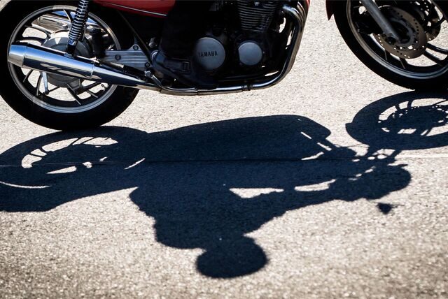 Ein Motorradfahrer und seine Maschine werfen Schatten auf den Asphalt.