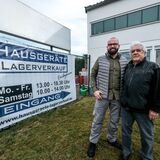 Tim Theisinger und Esmail Esmaili stehen vor einem Transparent, das den neuen Lagerverkauf von Hausgeräten in Recklinghausen ankündigt.