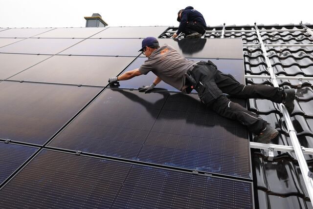 Handwerker montieren auf dem Dach eines Wohnhauses Solarmodule.