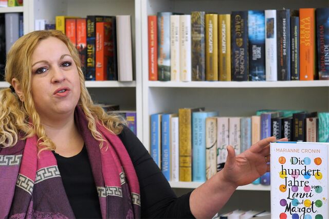 Buchhändlerin Britta Spengler sitzt vor einem Bücherregal und zeigt auf ein Buch.