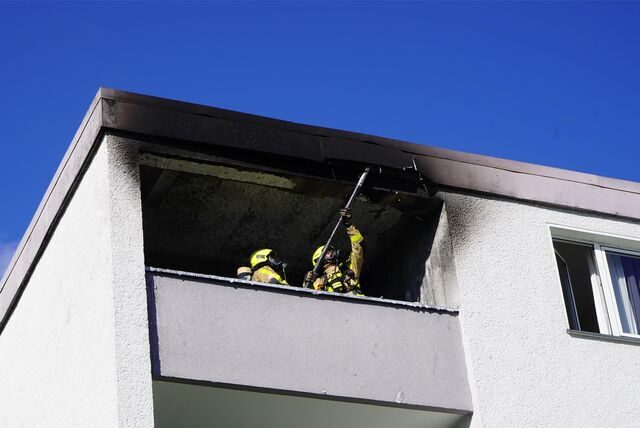 Feuerwehrleute stehen auf einer rußgeschwärzten Loggia.