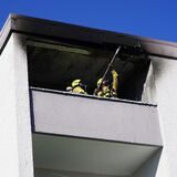 Feuerwehrleute stehen auf einer rußgeschwärzten Loggia.