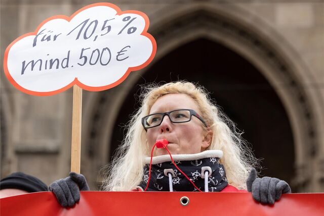 Eine Frau hält bei einem Warnstreik ein Schild mit einer Forderung