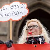 Eine Frau hält bei einem Warnstreik ein Schild mit einer Forderung
