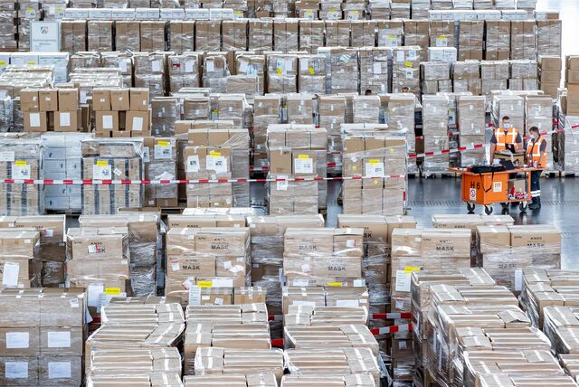 Mitarbeiter mit Schutzmasken arbeiten zwischen zahlreichen Kartons mit Schutzausrüstung in Millionenzahl.