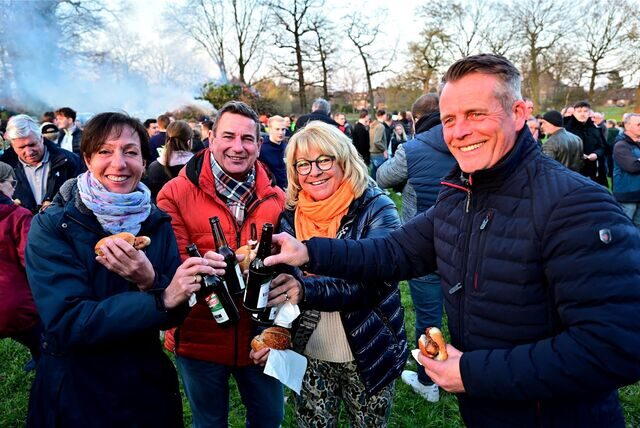 Vier Besucher des Osterfeuers in Recklinghausen-Speckhorn stoßen mit ihren Bierflaschen an, im Hintergrund qualmt das Feuer