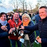 Vier Besucher des Osterfeuers in Recklinghausen-Speckhorn stoßen mit ihren Bierflaschen an, im Hintergrund qualmt das Feuer