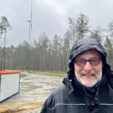 Dr. Bernhard Klocke steht am neu gebauten Windrad. Im Hintergrund ist das Windrad zu sehen, das gesprengt wird.