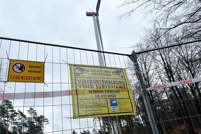 Ein Windrad steht auf einem Waldgelände, das mit Absperrgittern verriegelt ist.