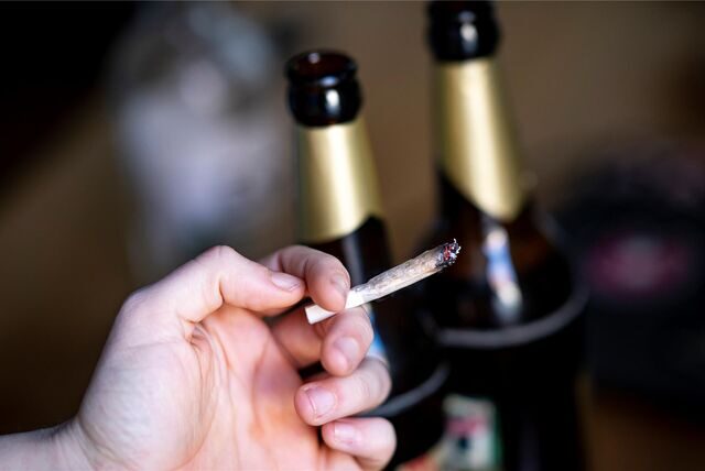 Eine Hand hält einen Joint, im Hintergrund zwei Flaschen Bier.