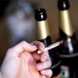 Eine Hand hält einen Joint, im Hintergrund zwei Flaschen Bier.