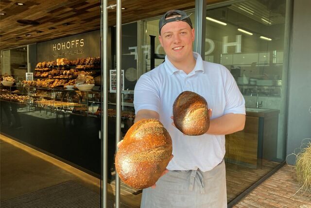 Ein Mann in weißem Polohemd und Schürze steht vor einer Bäckereifiliale in Waltrop. In den Händen hält er zwei Brote. (Archivbild)