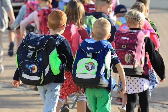 Kinder sind auf dem Weg zur Schule von hinten zu sehen. Sie tragen große Schulranzen auf dem Rücken.