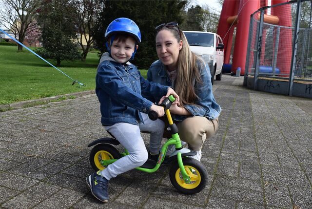 Ein Kind sitzt auf einem Tretfahrrad, dahinter hockt die Mutter