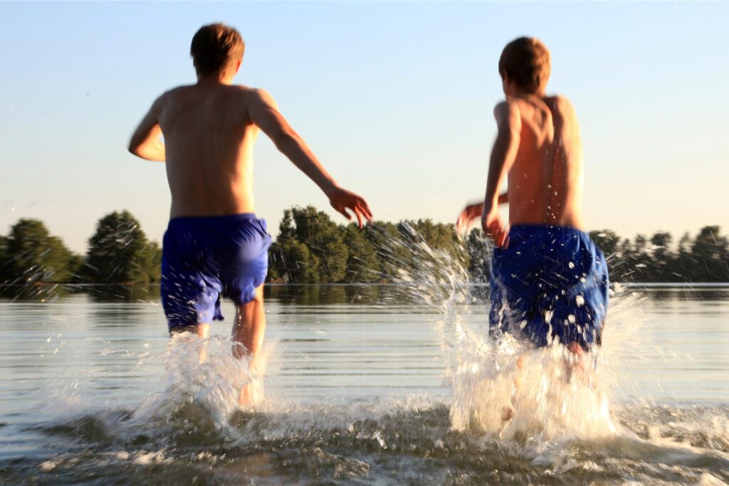 Zwei Jungen rennen in das Wasser eines Sees